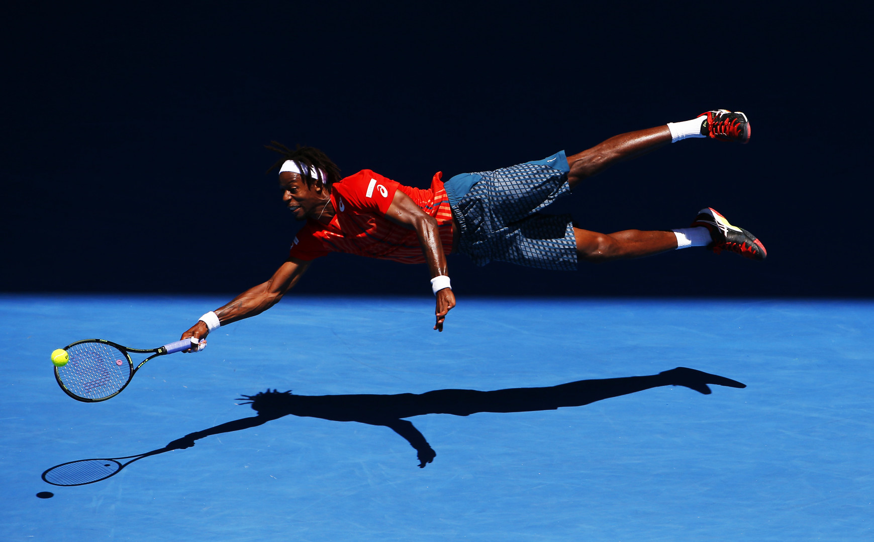 Male tennis player launching himself across the court to reach the tennis ball with his racquet.