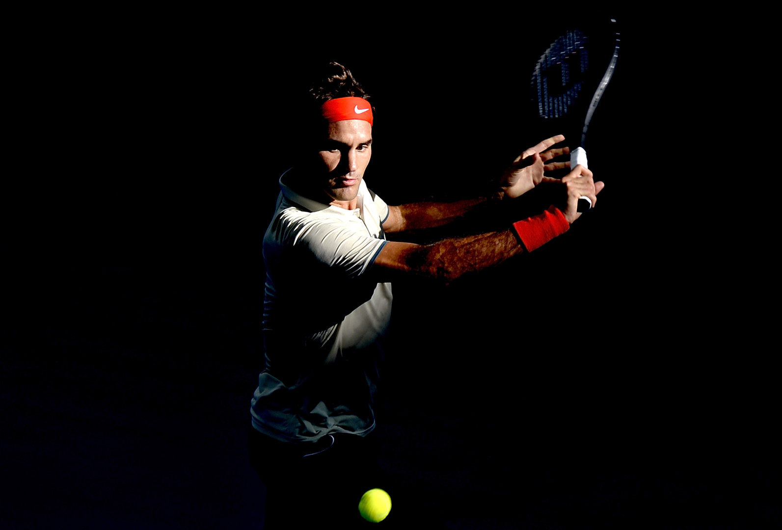 Roger Federer appearing into the light to hit a tennis ball.