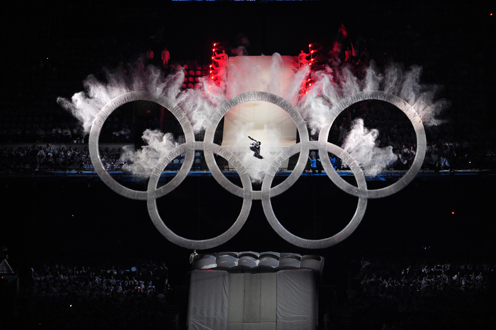 Snowboarder bursting through the middle of the Olympic rings at the Winter Olympic ceremony.