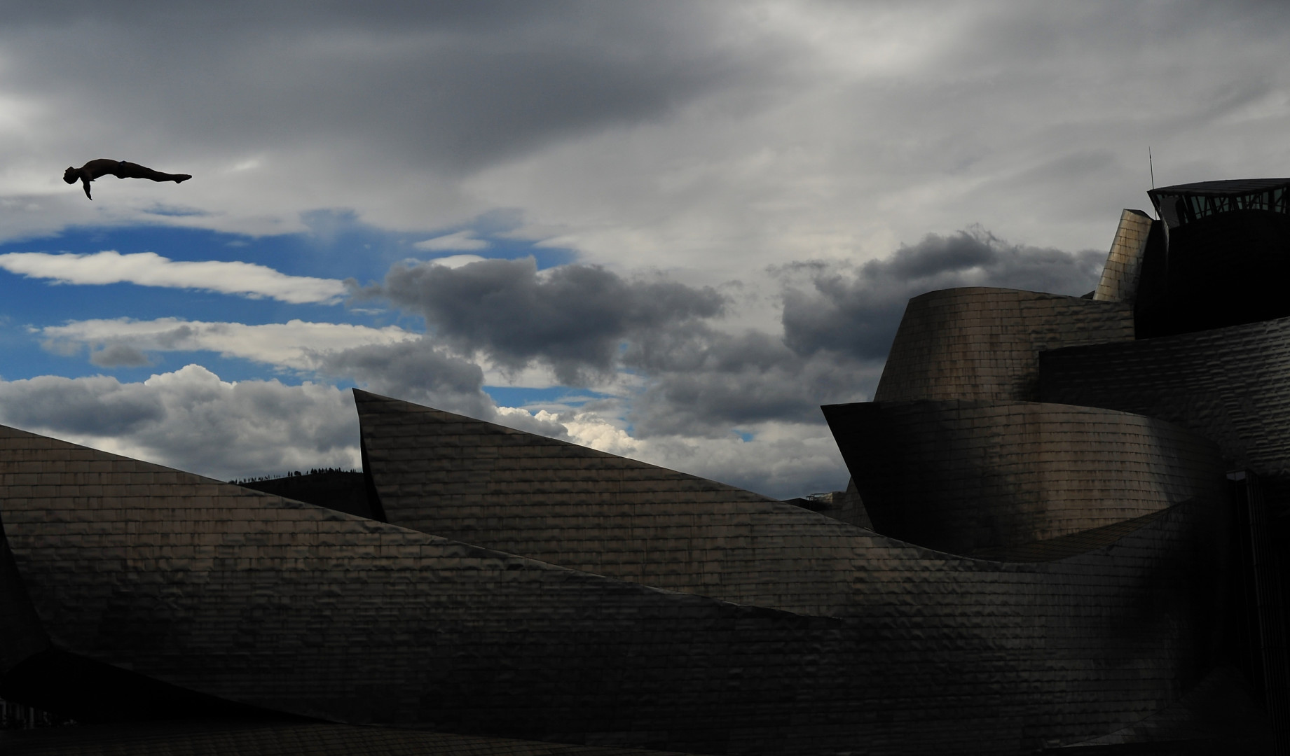 Freestyle diver mid air as they dive in front of modern buildings.