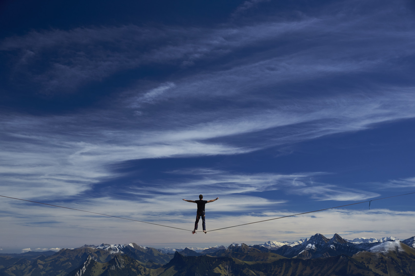 A man walking a tightrope whilst enjoying the mountainous view.