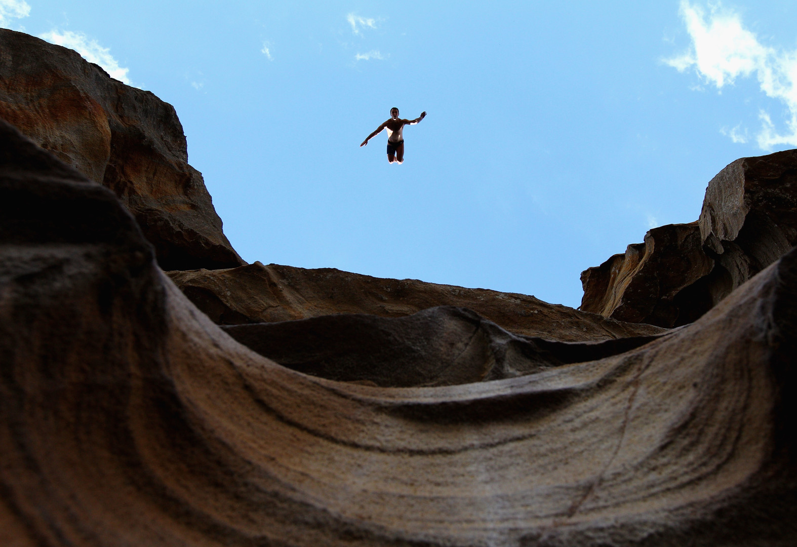 Man cliff diving off canyon-like cliff side.