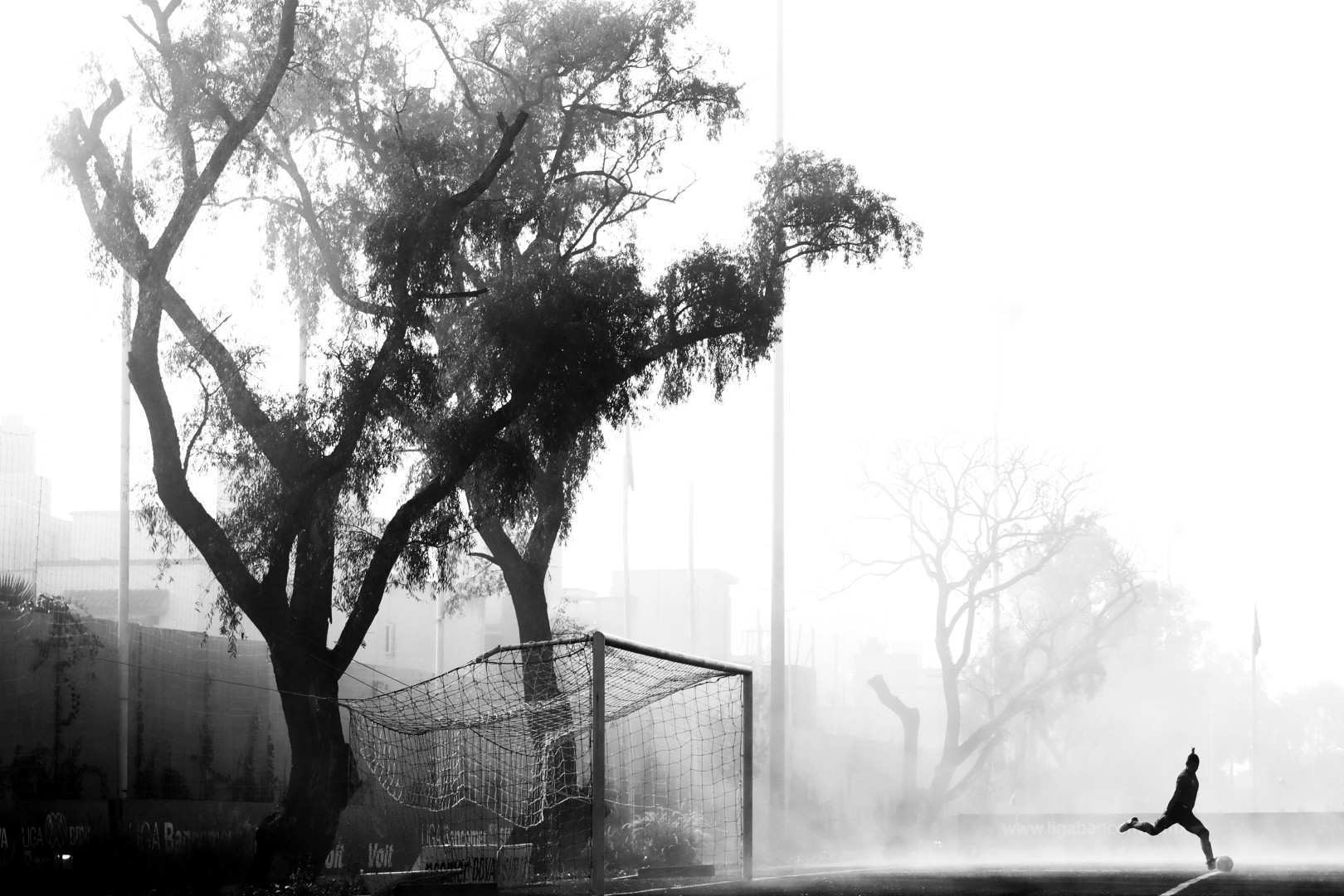 Black & White image of young footballer kicking football away from goal in the mist.