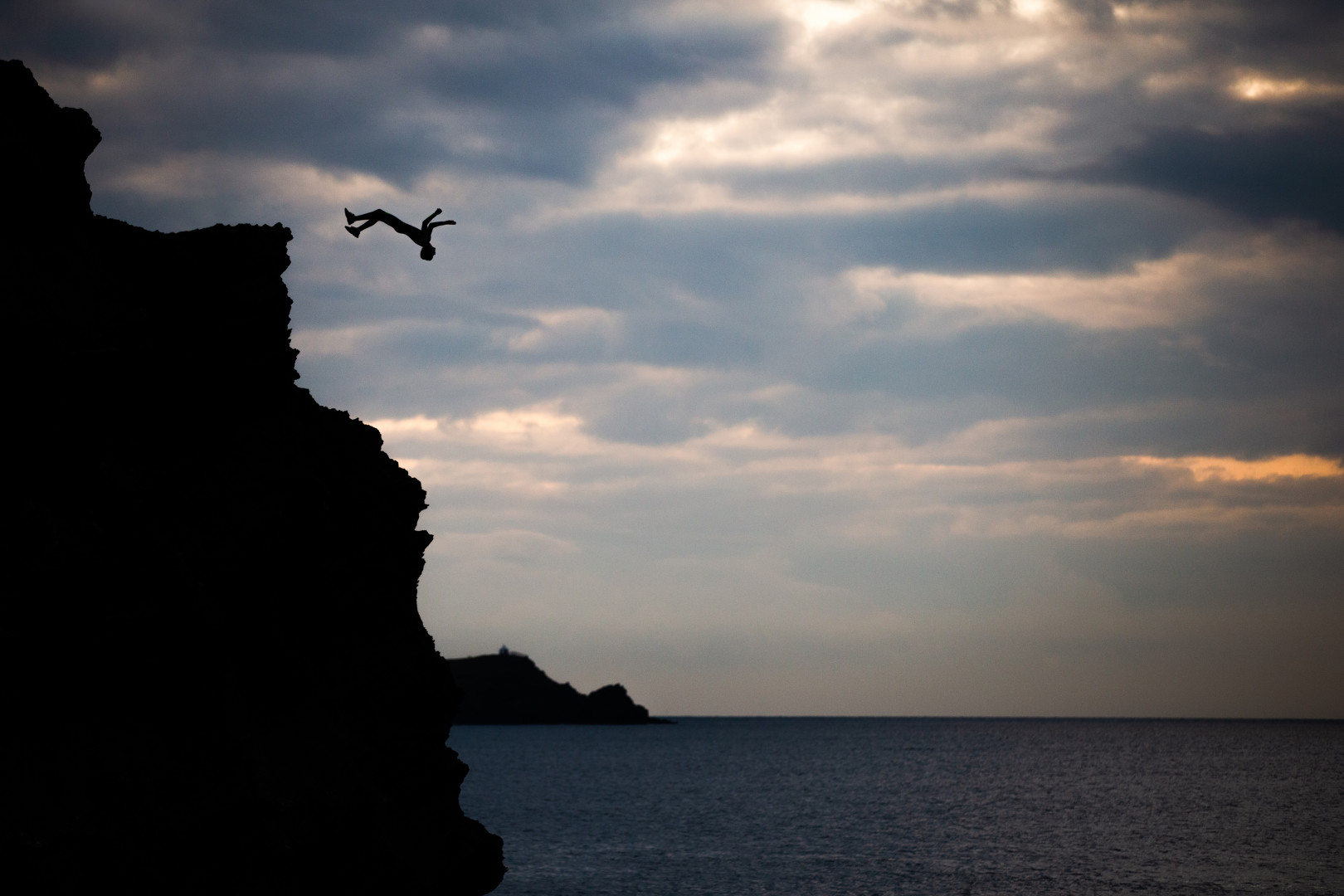Silhouette thirteen year old backflipping off of cliff into the sea.