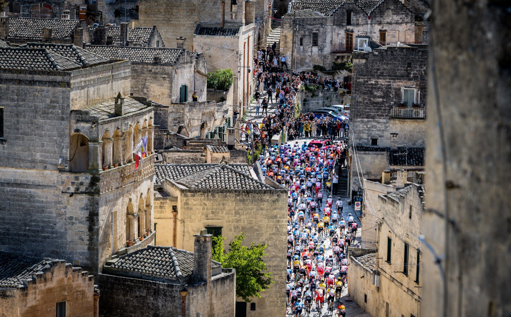 Group of cyclists riding through narrow streets of city.