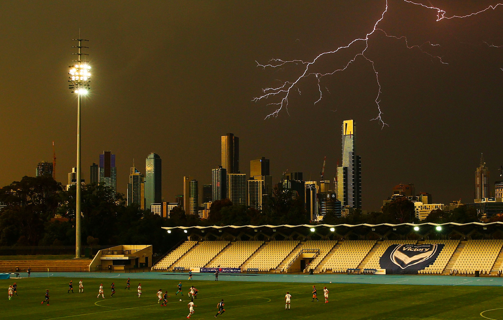Strike of lighting through the dark grey sky as women's football game takes place at stadium.