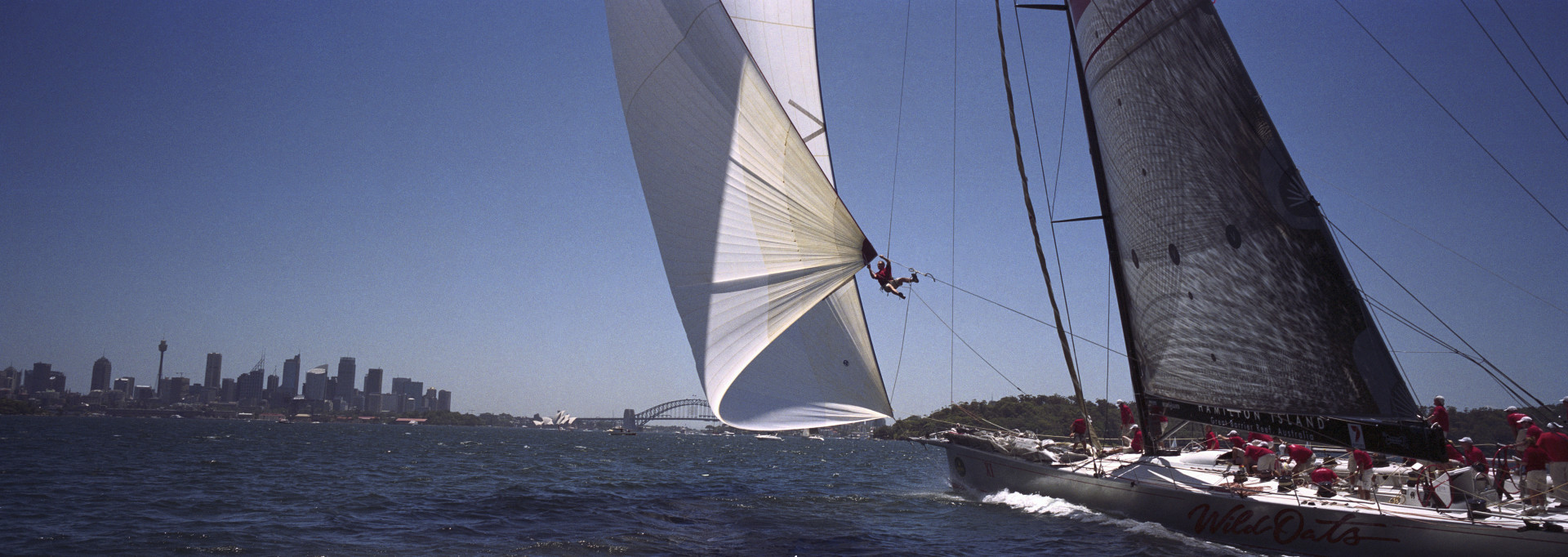 Bowman Sven Ruenow attaches the drop line to the spinnaker onboard as boat sails at Big Boat Challenge on Sydney Harbour.