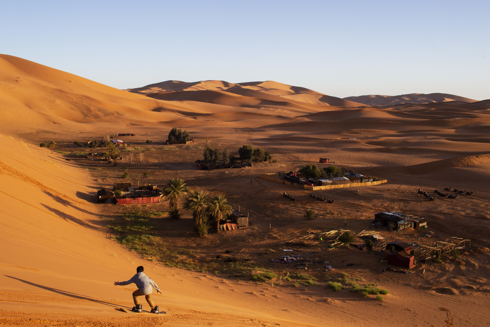 Young boy boarding down a sand dune in the desert.