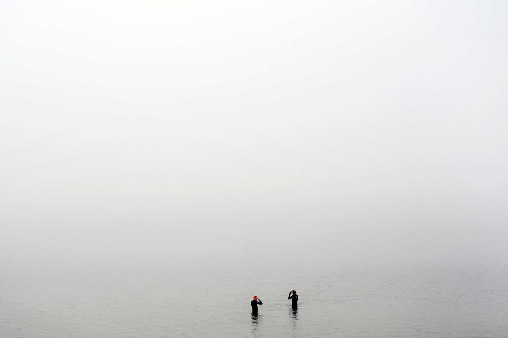 Two cold water swimmers preparing to immerse themselves in the cold water and foggy conditions.