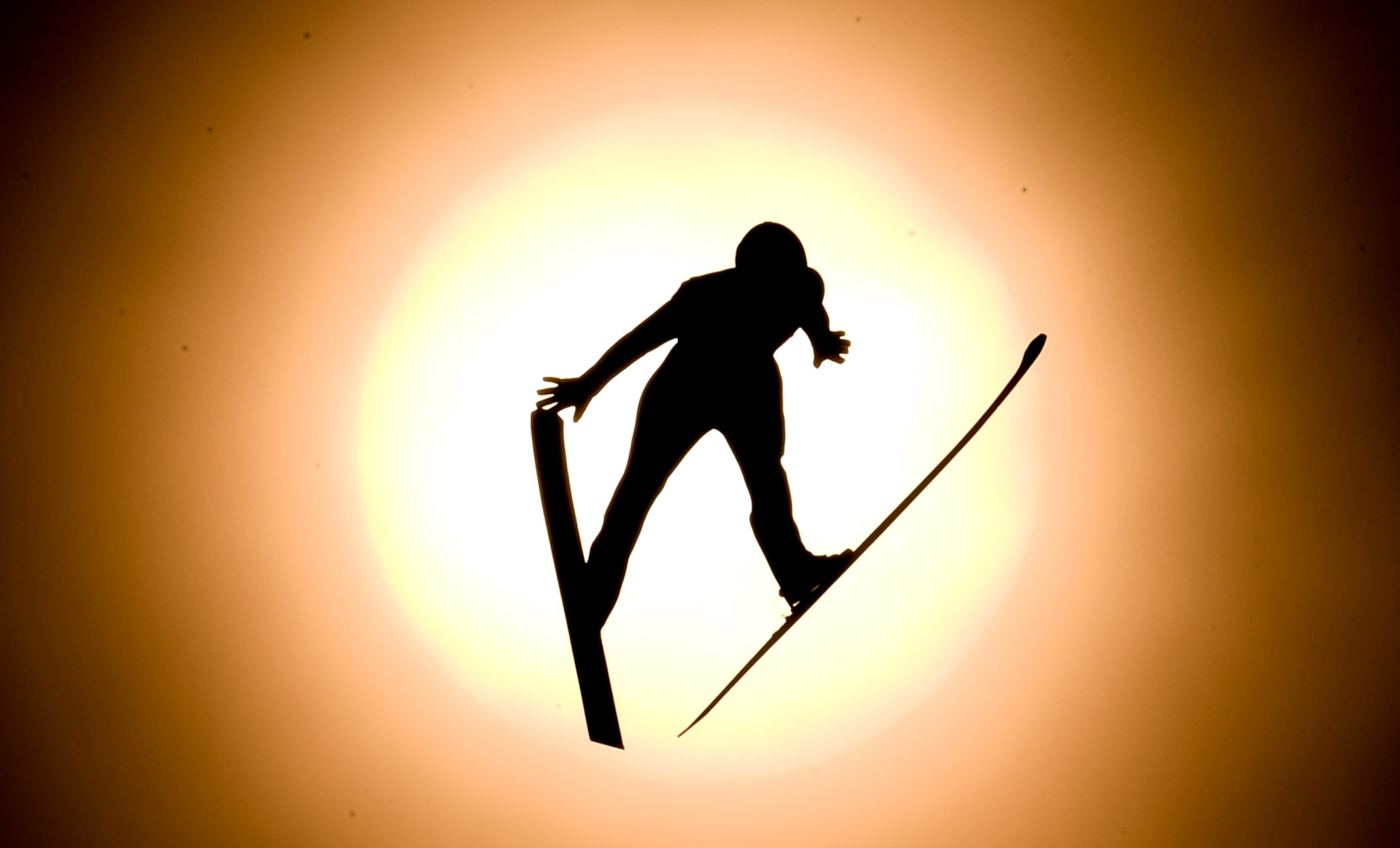 Silhouette of Ski Jumper in front of the sun mid jump.