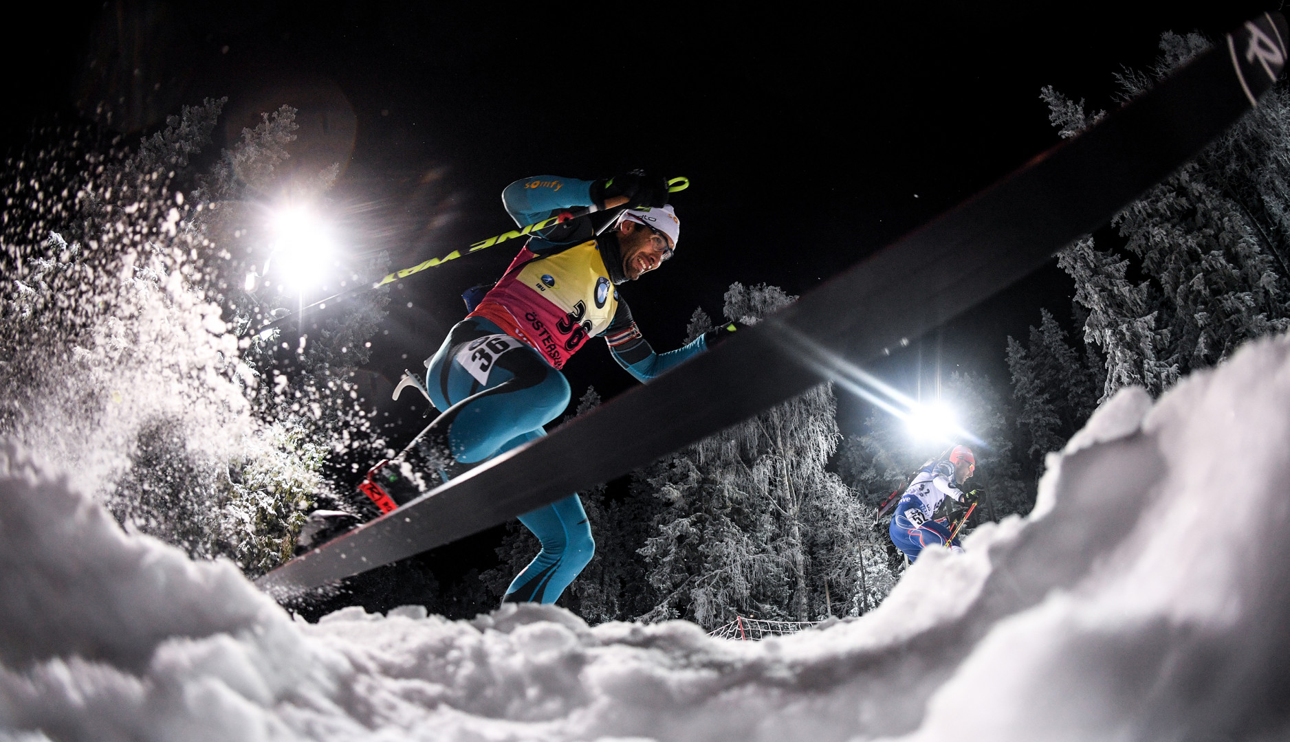 Below photograph of two biathlon skiers battling through the snow.