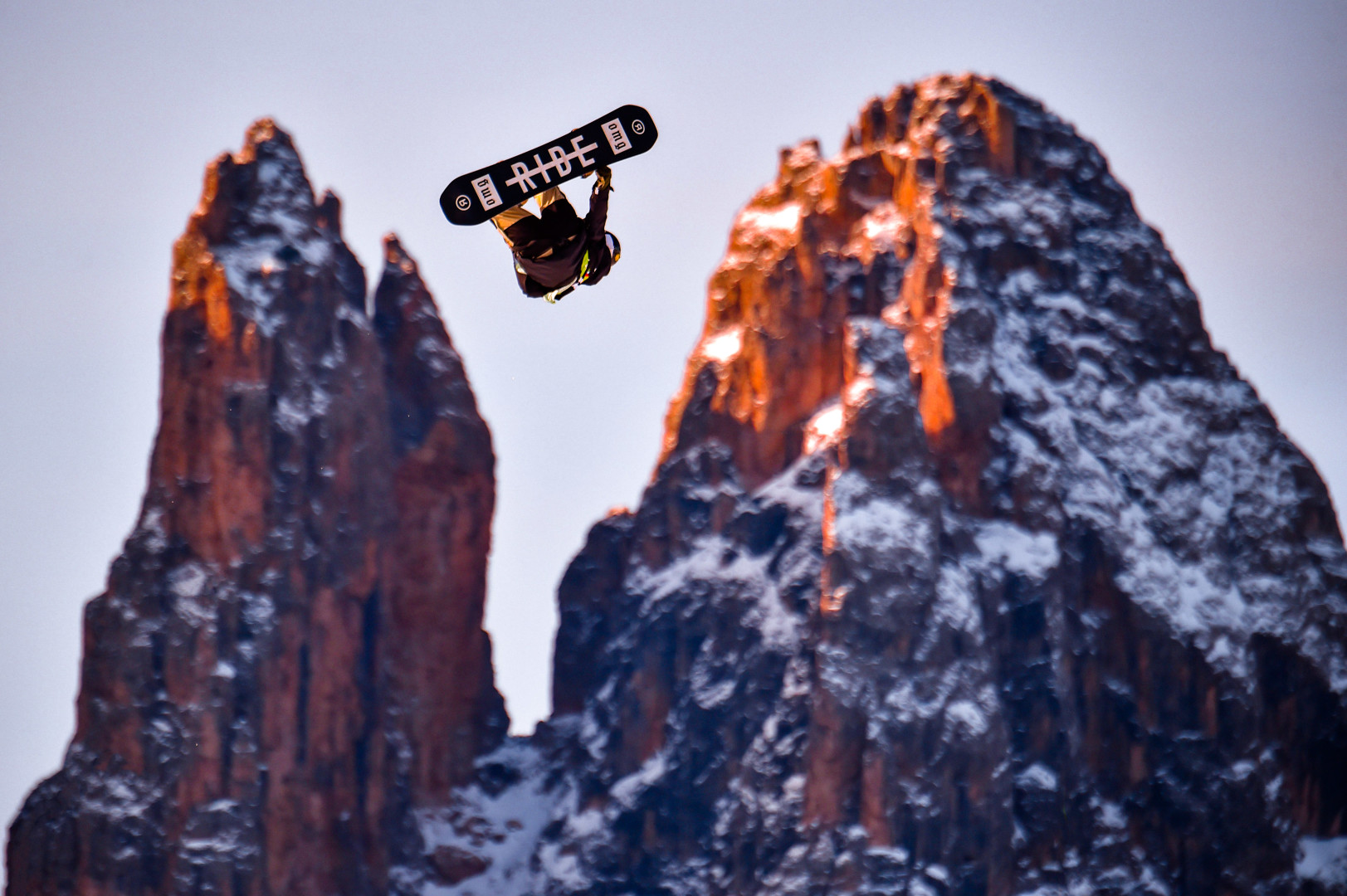 Snowboarder mid air during trick in between the dolomite mountains.