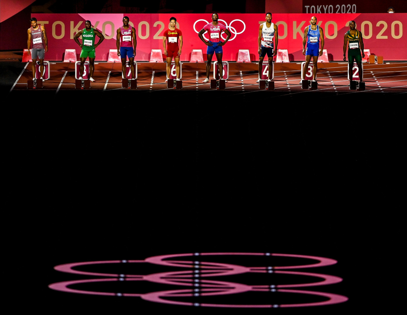 Spotlight of athletes waiting for start of race as the Olympic logo is projected onto the track.