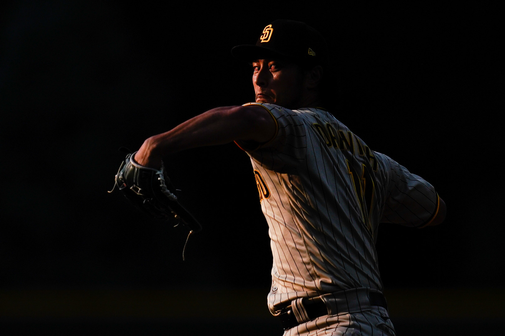 Light catching the figure of a bloodshot pitcher in the movement of throwing the ball.