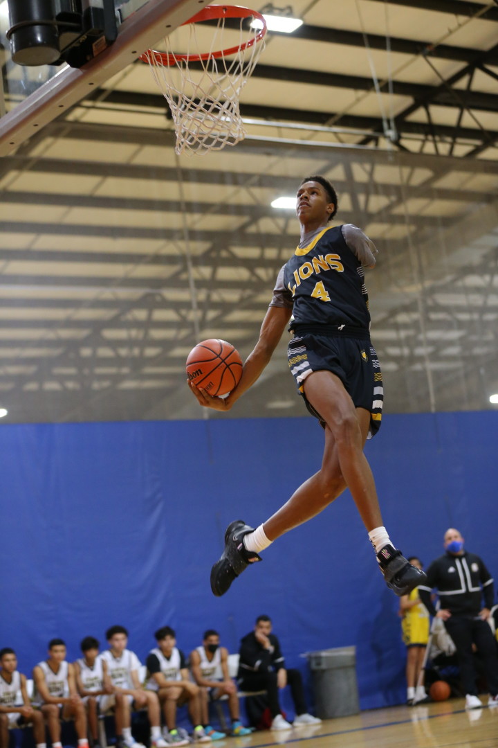 Young Lions basketball player mid air, jumping for a slam dunk.