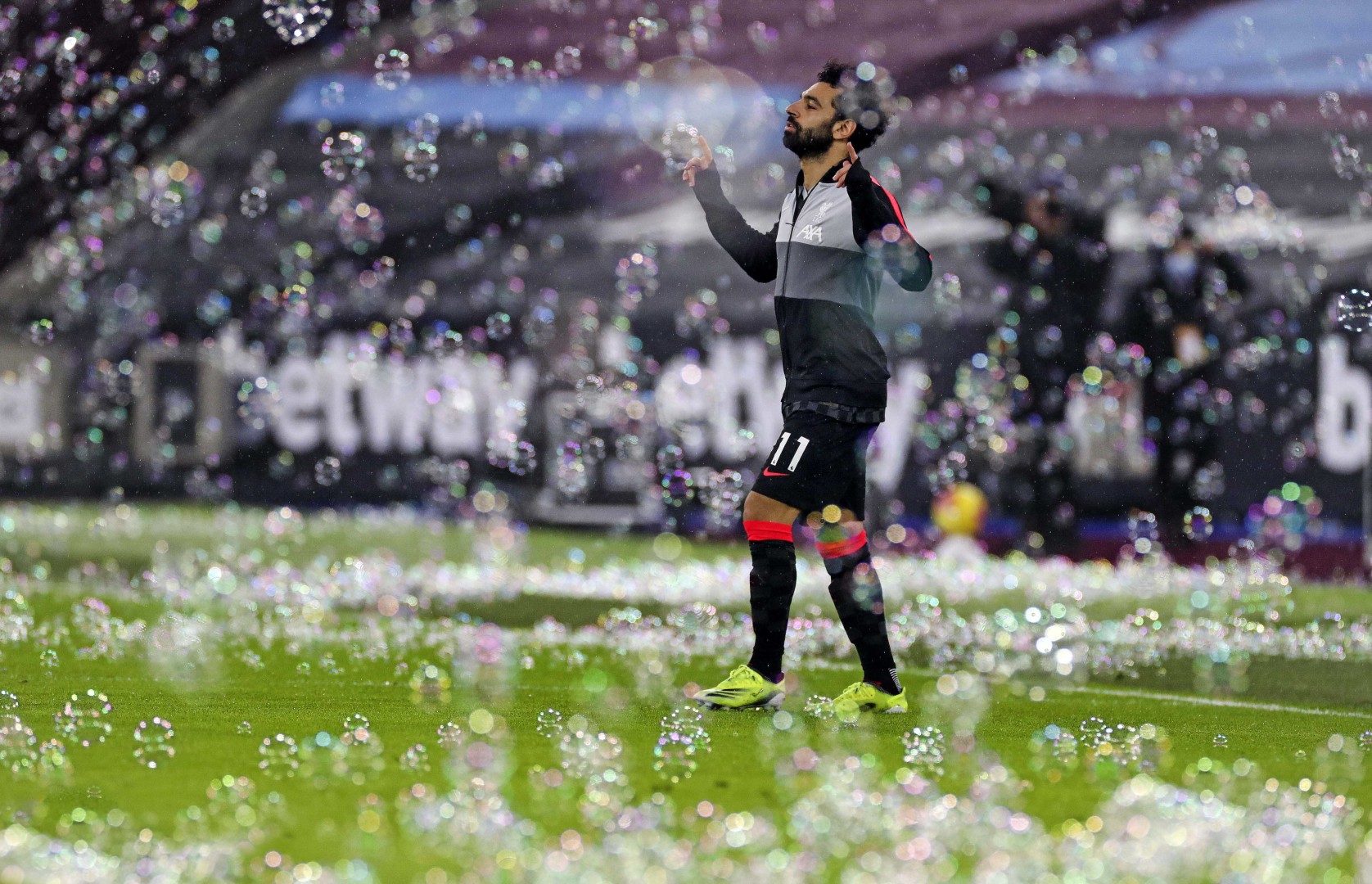 Mo Salah pointing to the sky as he walks across the pitch immersed in bubbles.