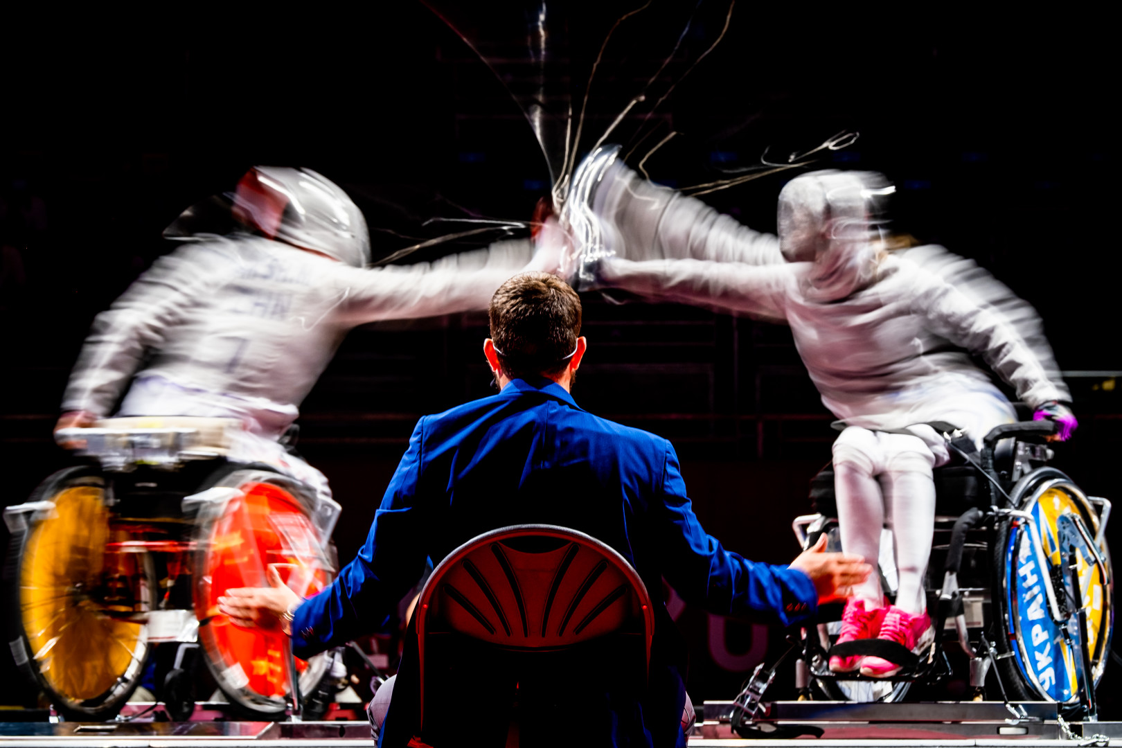 Wheelchair fencing competitors in a blur of action as static judge watches on.