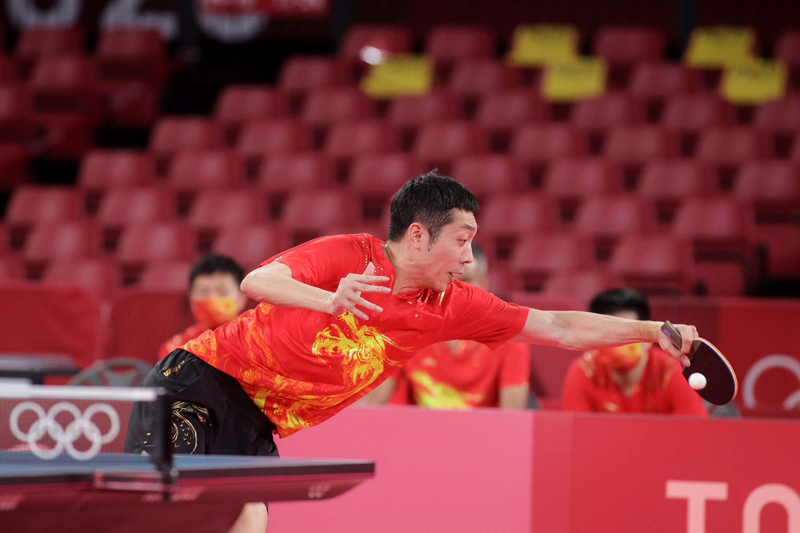 Chinese table tennis competitor reaching wide to stop ball flying off the table at the 2020 Tokyo Olympics.