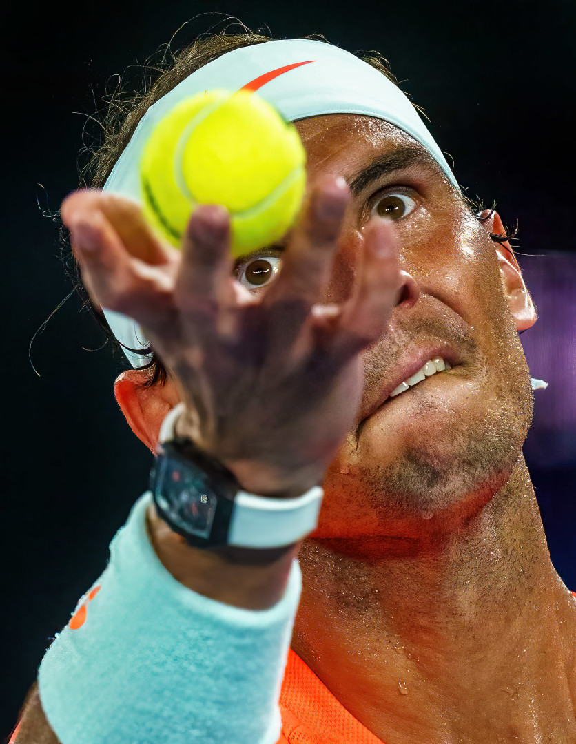 Close up portrait image of Rafael Nadal mid serve as he watches the tennis ball leave his hand.