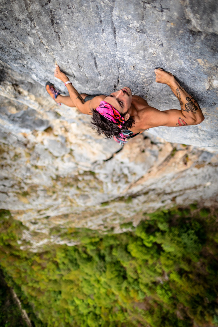 Man clinging on to rock face as he boulders up vertical cliff.