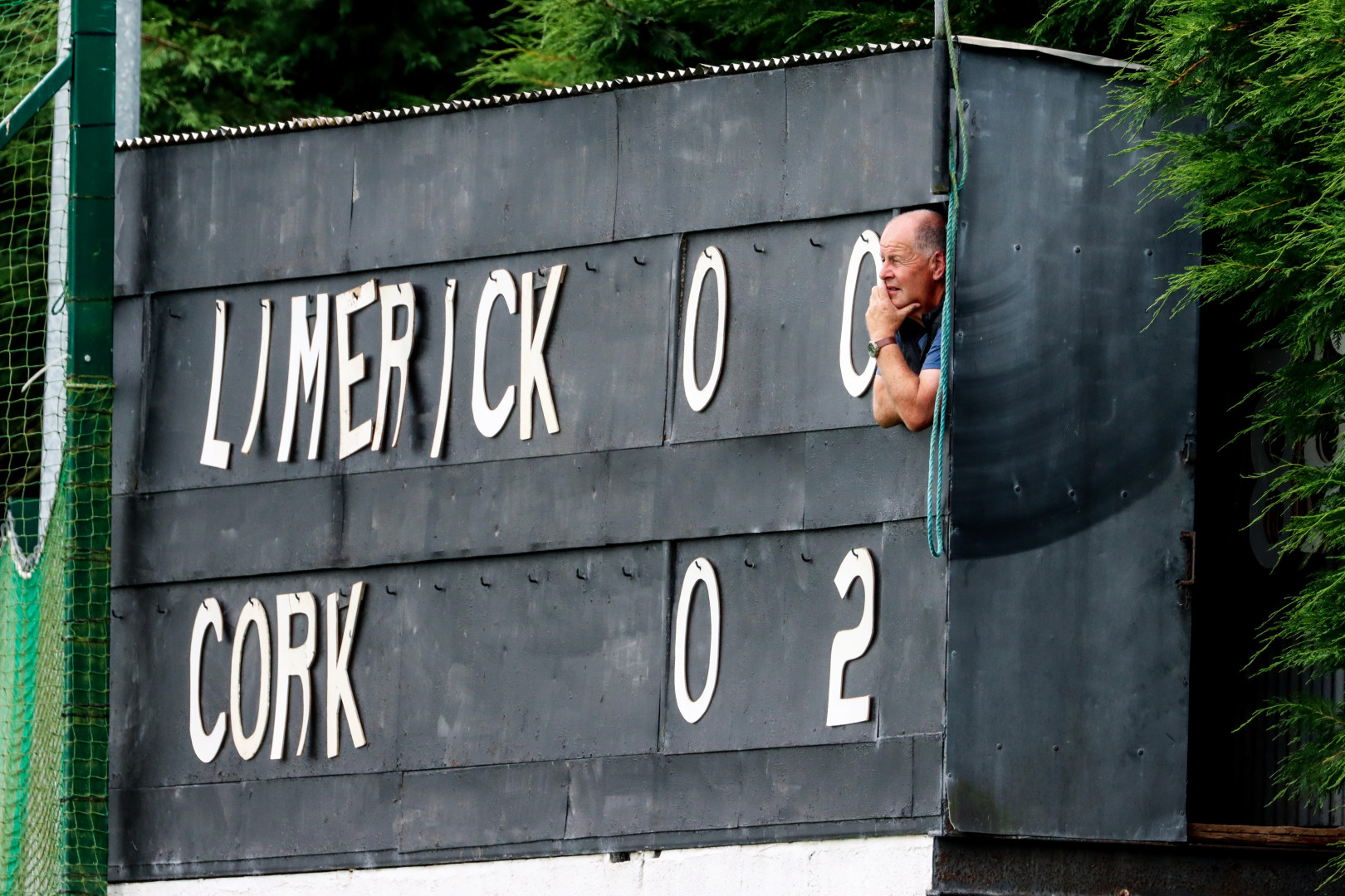 Man peering out of the old-style score board house as he watches ongoing sports game between Limerick and Cork.