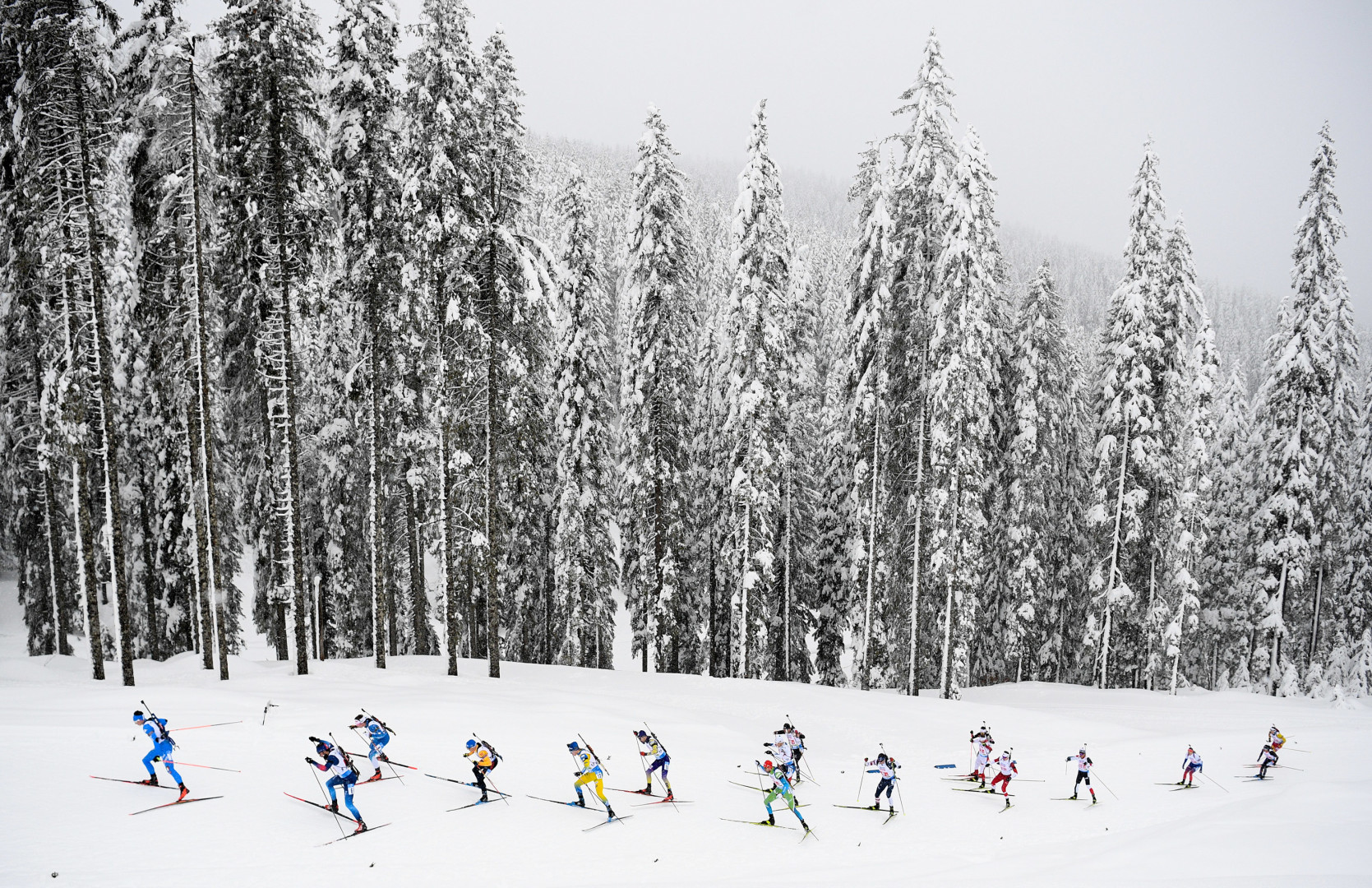 A trail of Biathletes skiing up a track in the cross-country ski section of sport.