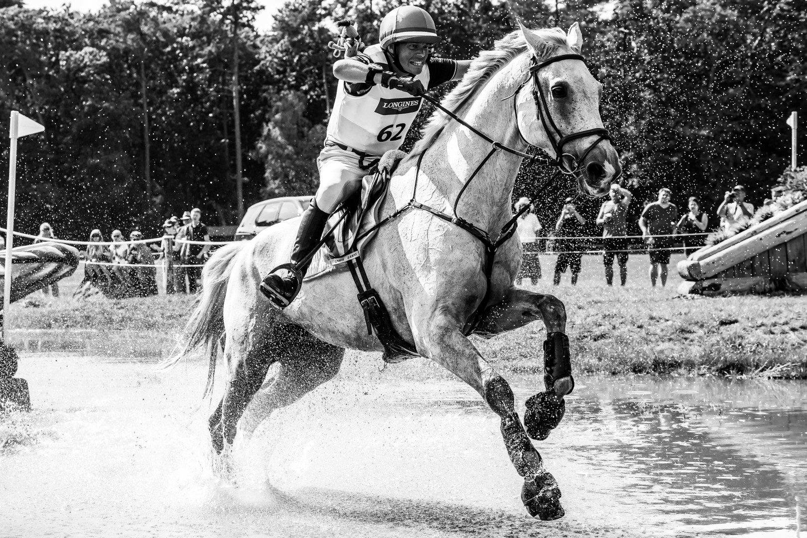 Black & White photograph of a jockey riding their horse through a water pit of the race course.
