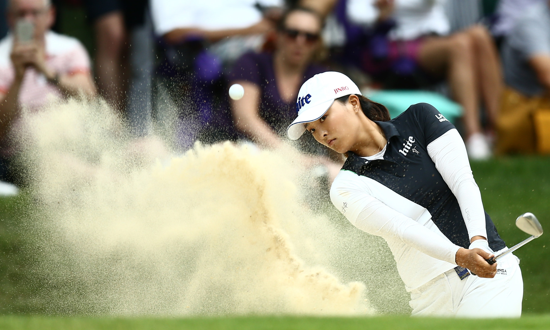 Ji Young Ko hitting the ball out of a bunker on the 17th green of a golf course.