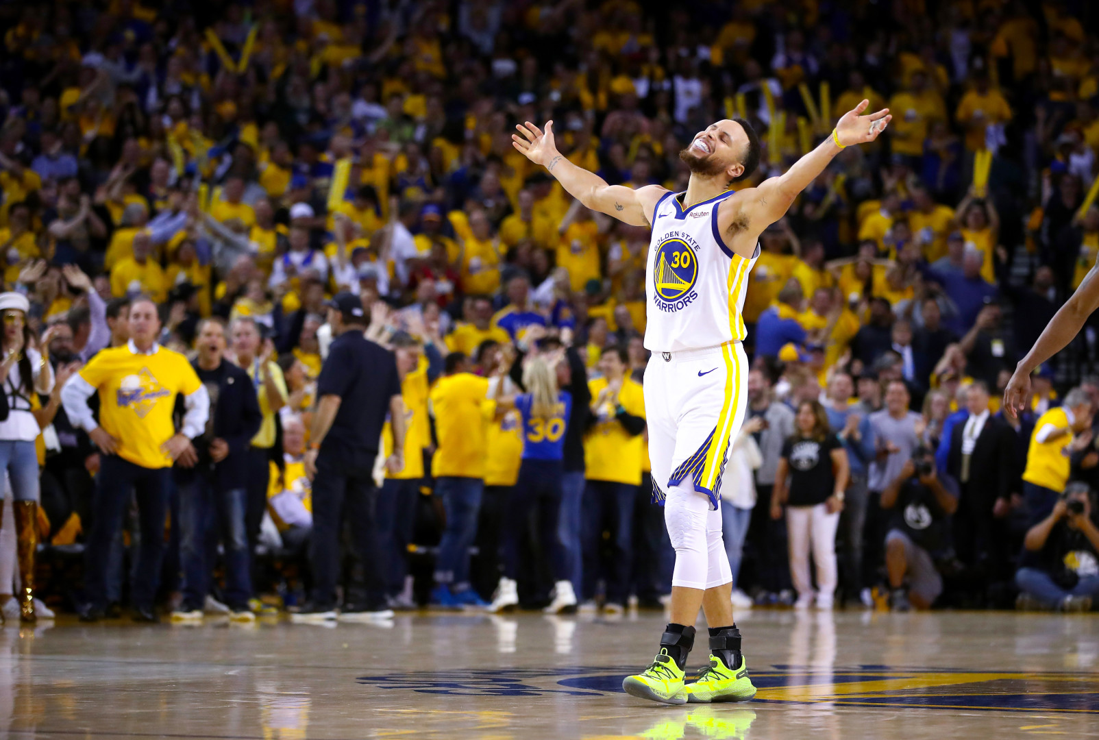Stephen Curry smiling with his arms in the air as Golden State Warriors win basketball match.