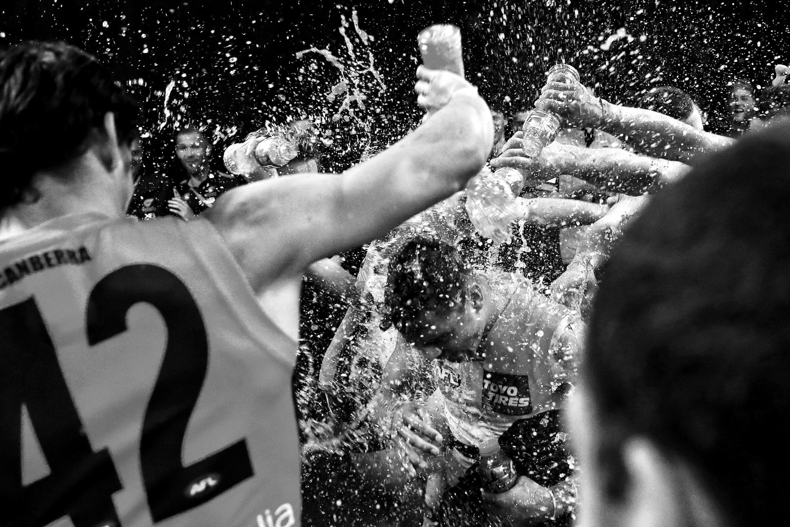 Black & White photograph of a new team mate being initiated into the sports team by being showered with bottles of water.