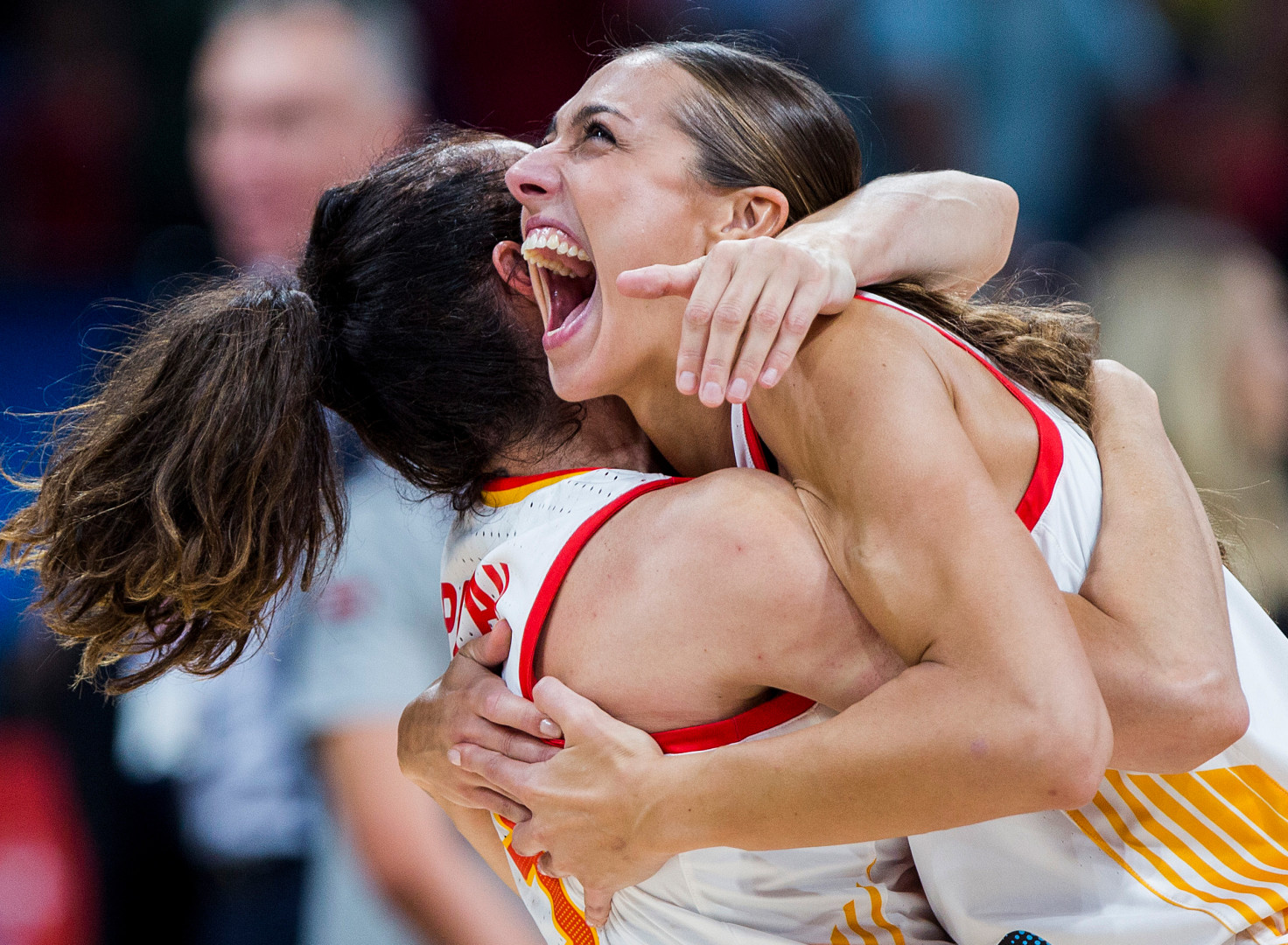 Elated female basketball players embrace in hug as they win a match.
