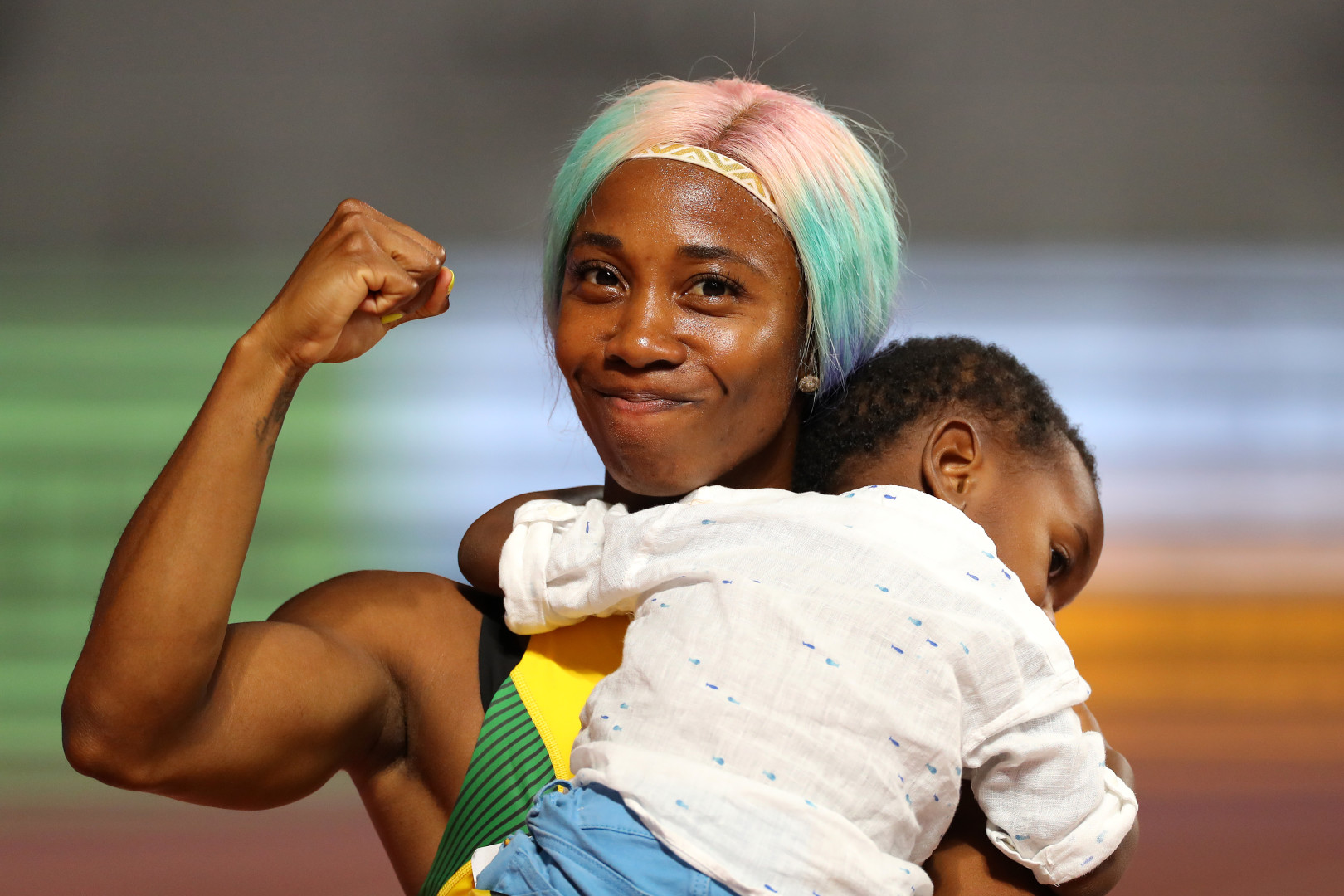 Shelly-Ann Fraser-Pryce celebrating race with clenched fist as she holds her young son in her arms.