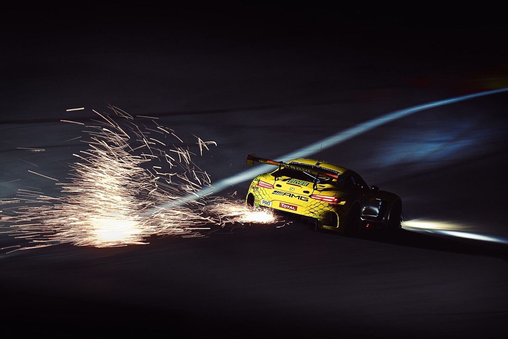 Sparks flying out onto the track from the back of a yellow race car.