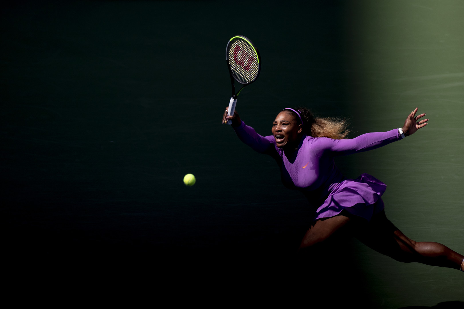Serena Williams in purple sports gear, smashing the tennis ball at 2019 US Open Tennis Tournament.