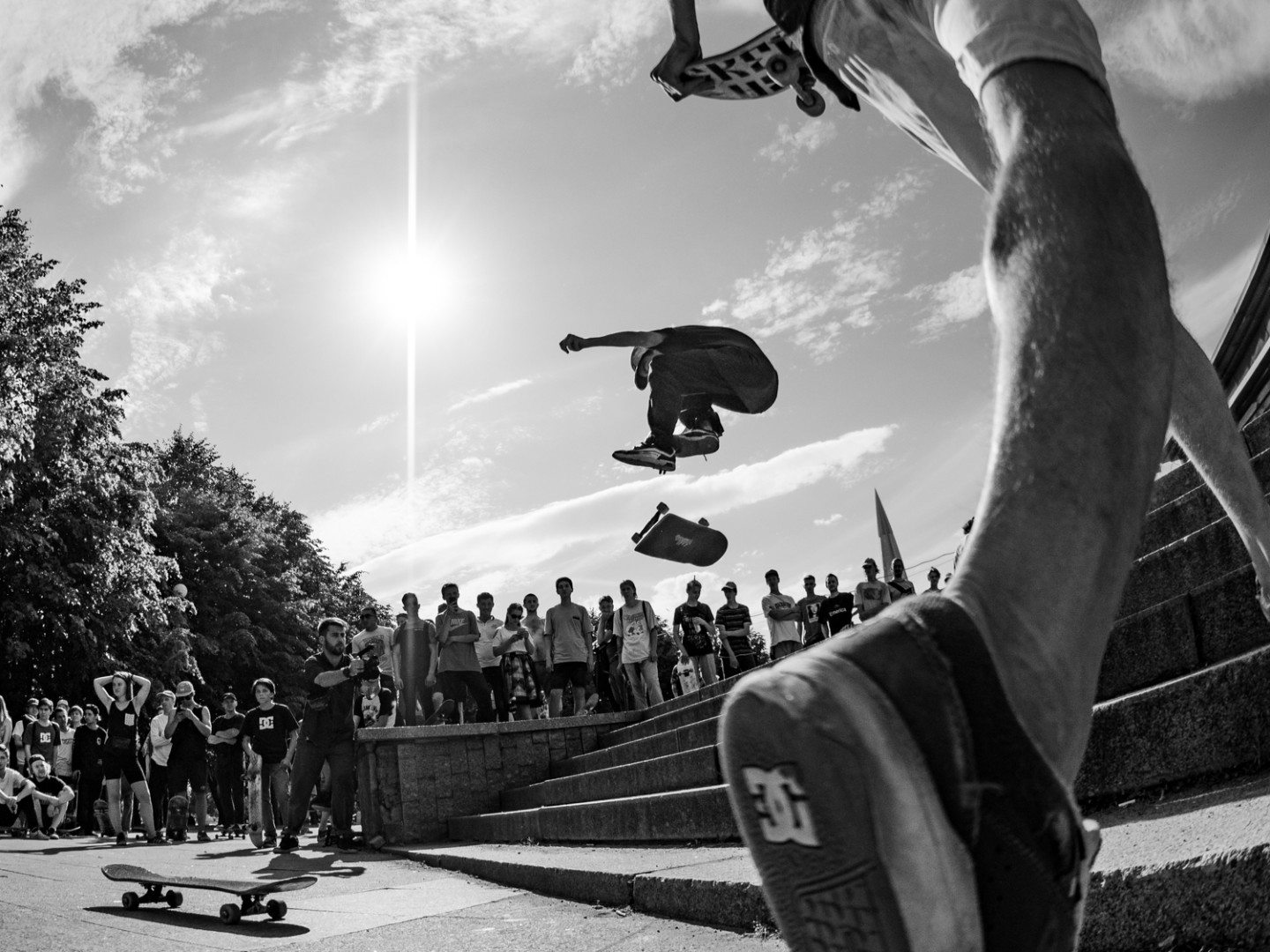 Fisheye photograph of a young skateboarder jumping a set of stairs as a group of other skaters watch.