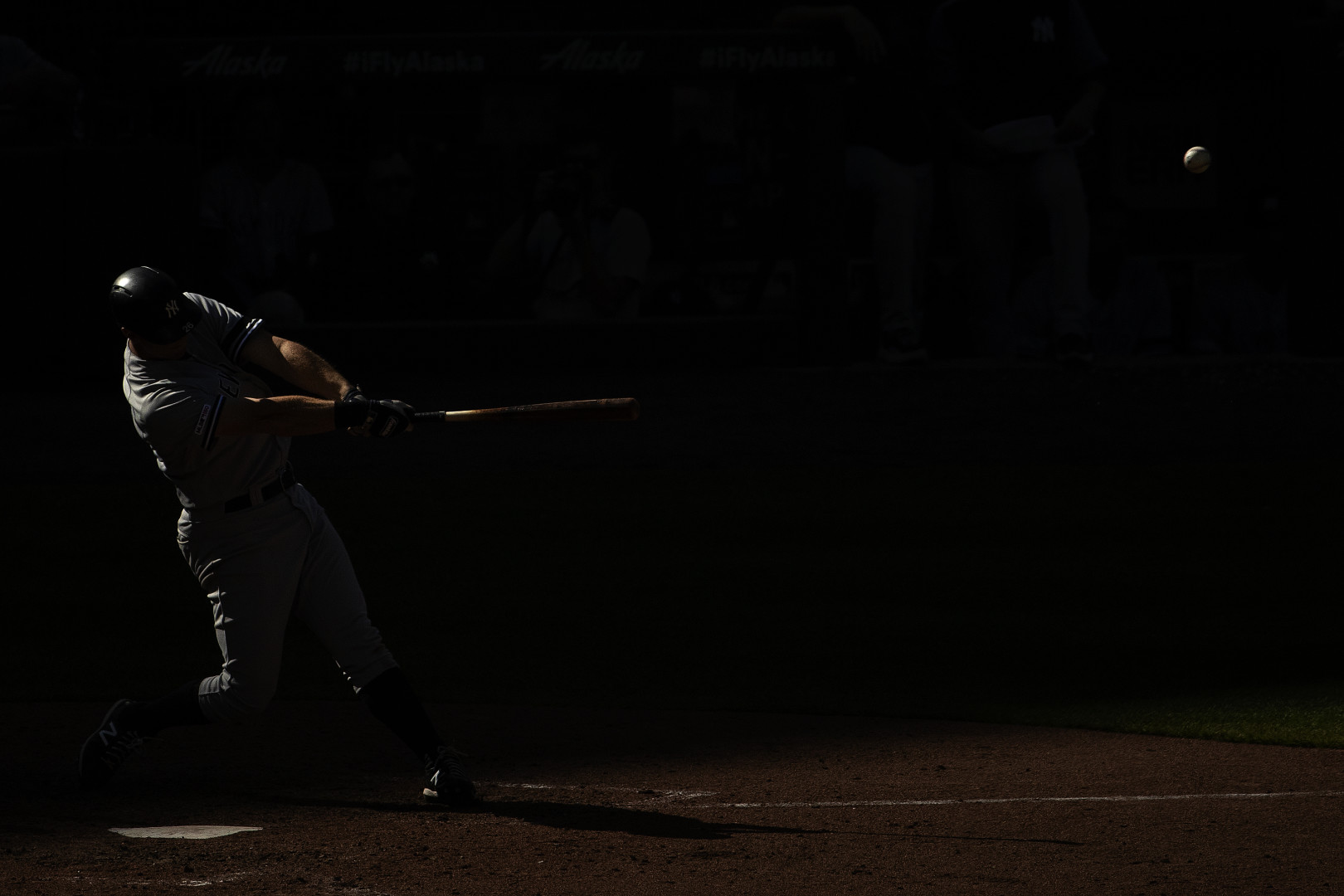 Dark photograph of the light catching the figure of a baseball player smashing a hit during a baseball game.