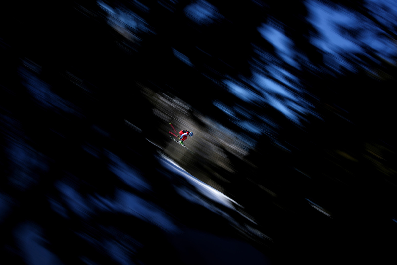 Alpine skier flying through the trees in motion after they jump ramp.