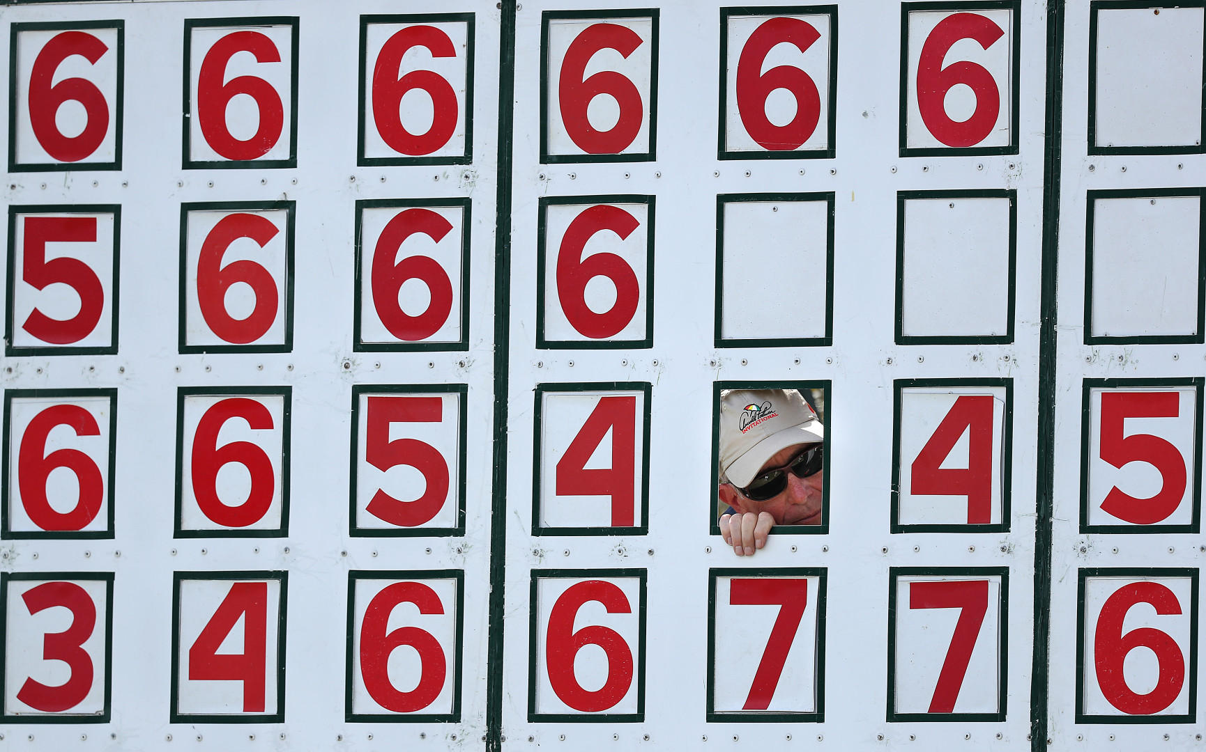 Spectator peering out of a cutout in a old-style scoreboard during sports game.