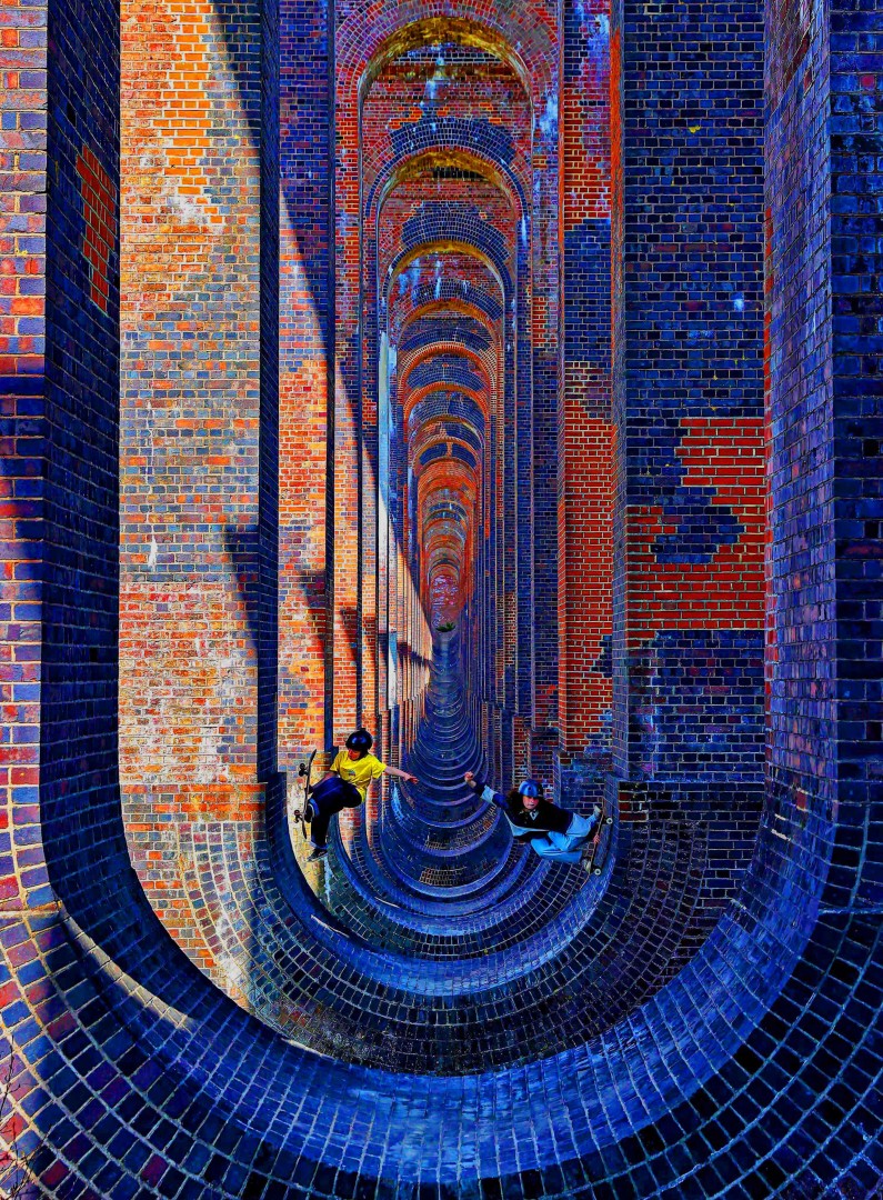 Young skateboarders using the underside structures of a viaduct to perform skate tricks.
