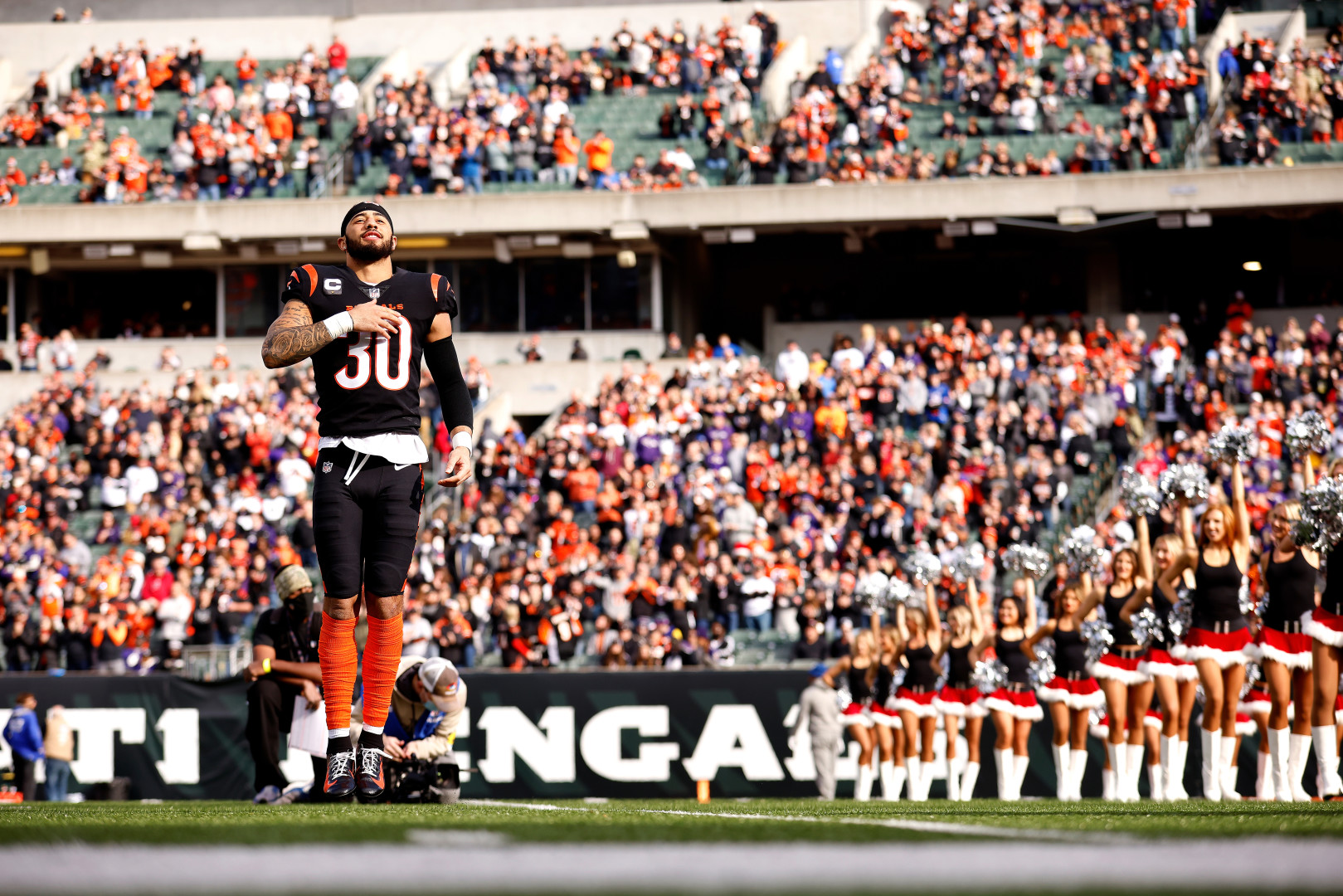 American Football player jumping in the air on the sidelines with his hand on his chest.