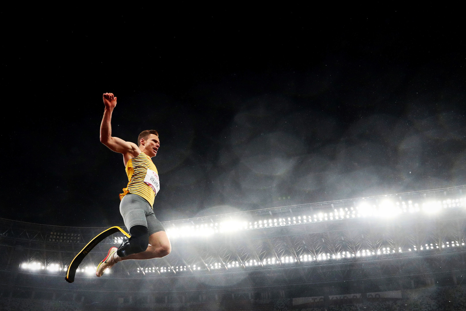 Male Paralympic long jumper flying through the air as the stadium lights shine behind him.