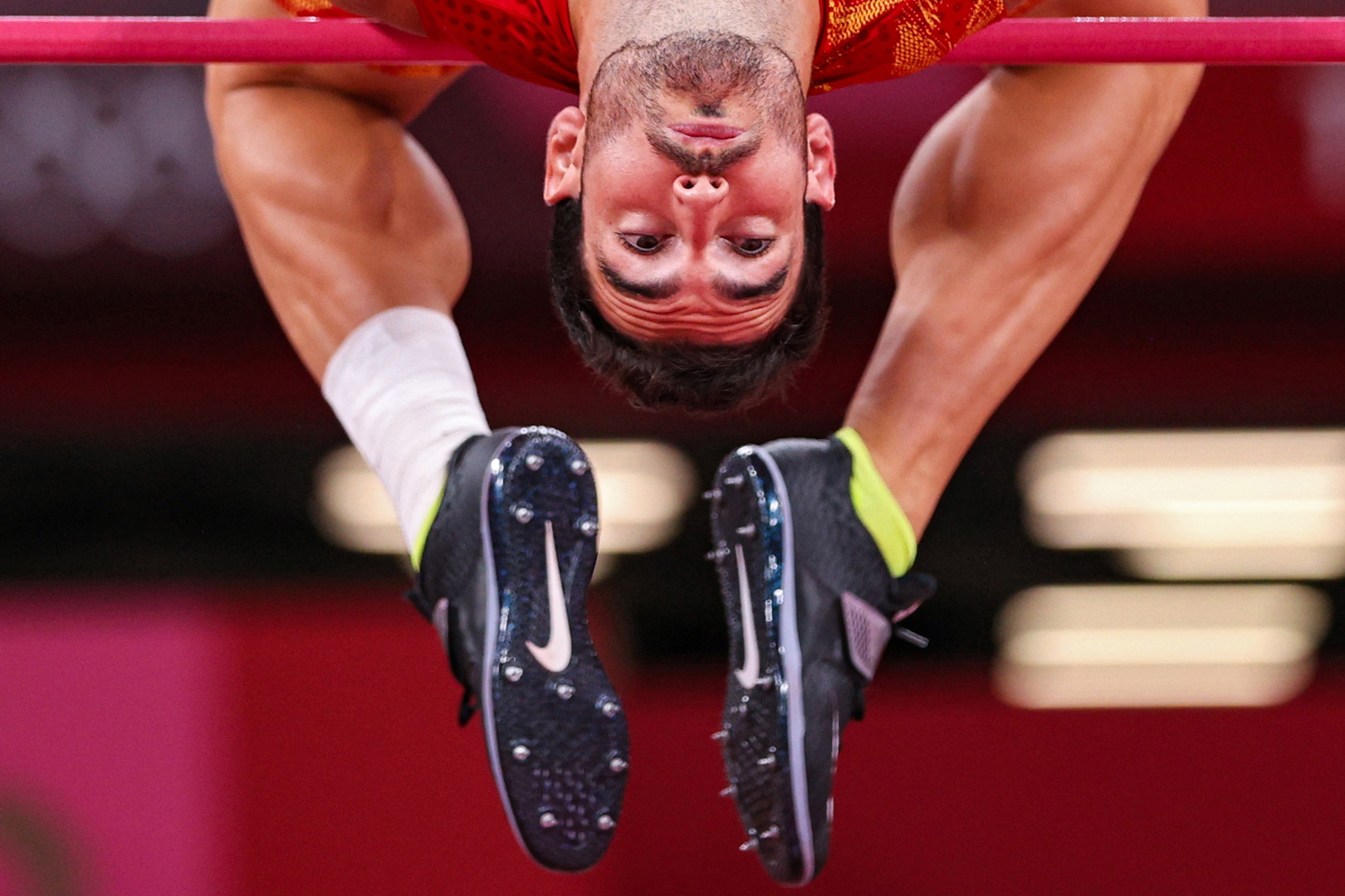 Male high jumper upside down as he  jumps over the high bar.