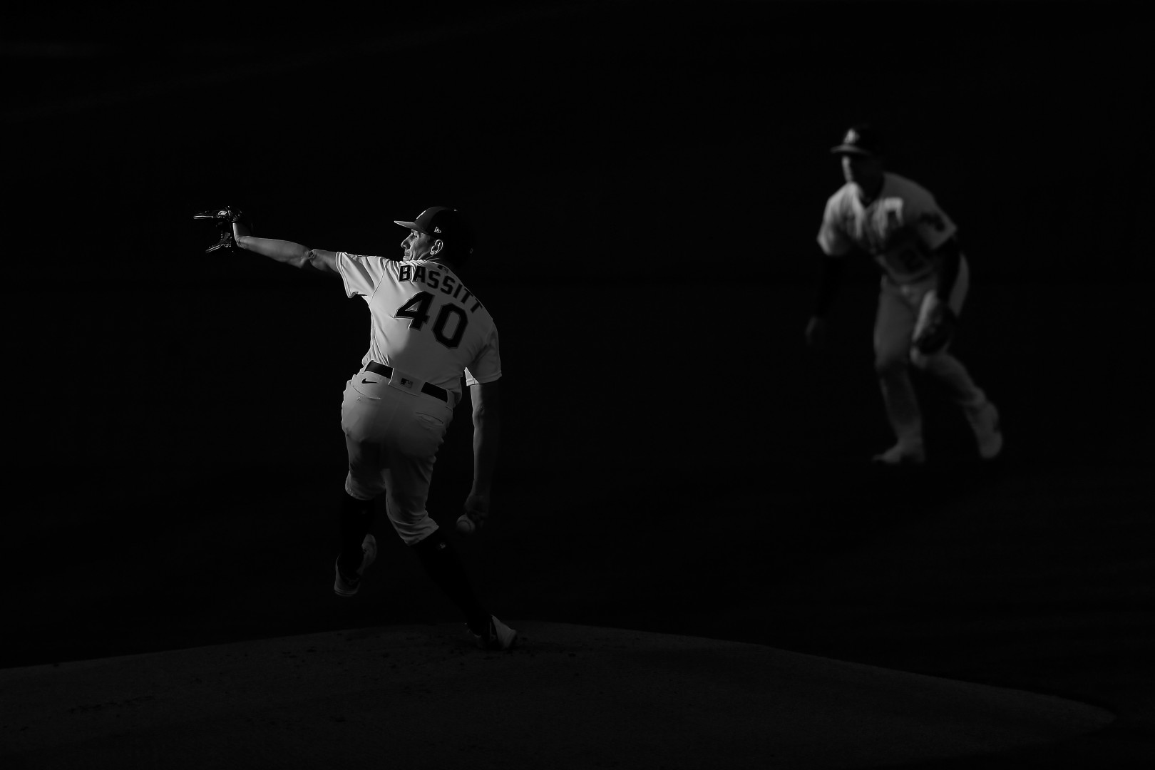 Black & White photograph of Chris Bassitt making his first pitch of the baseball game in the last light of the evening.