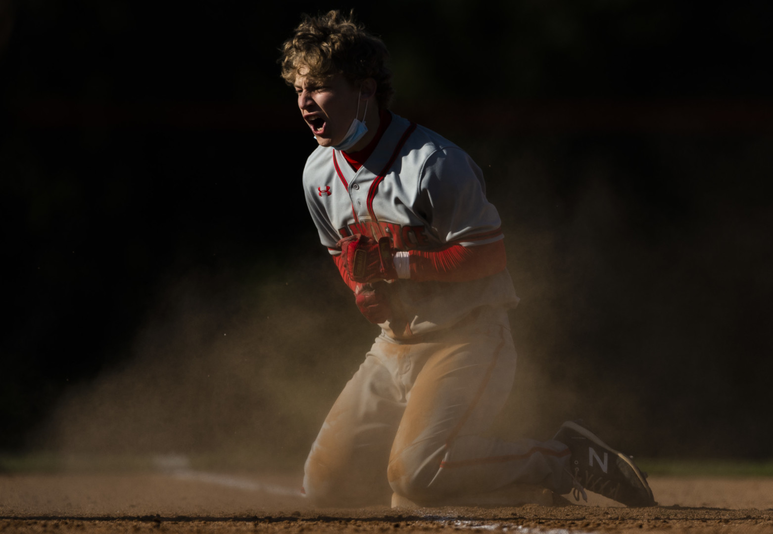 Baseball player on his knees on the dusty baseball pitch, yelling with joy.