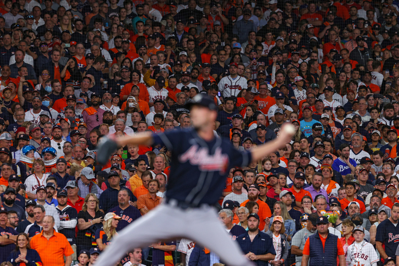 Baseball pitcher throwing the ball out of focus as the crowd's reactions behind are captured in focus.