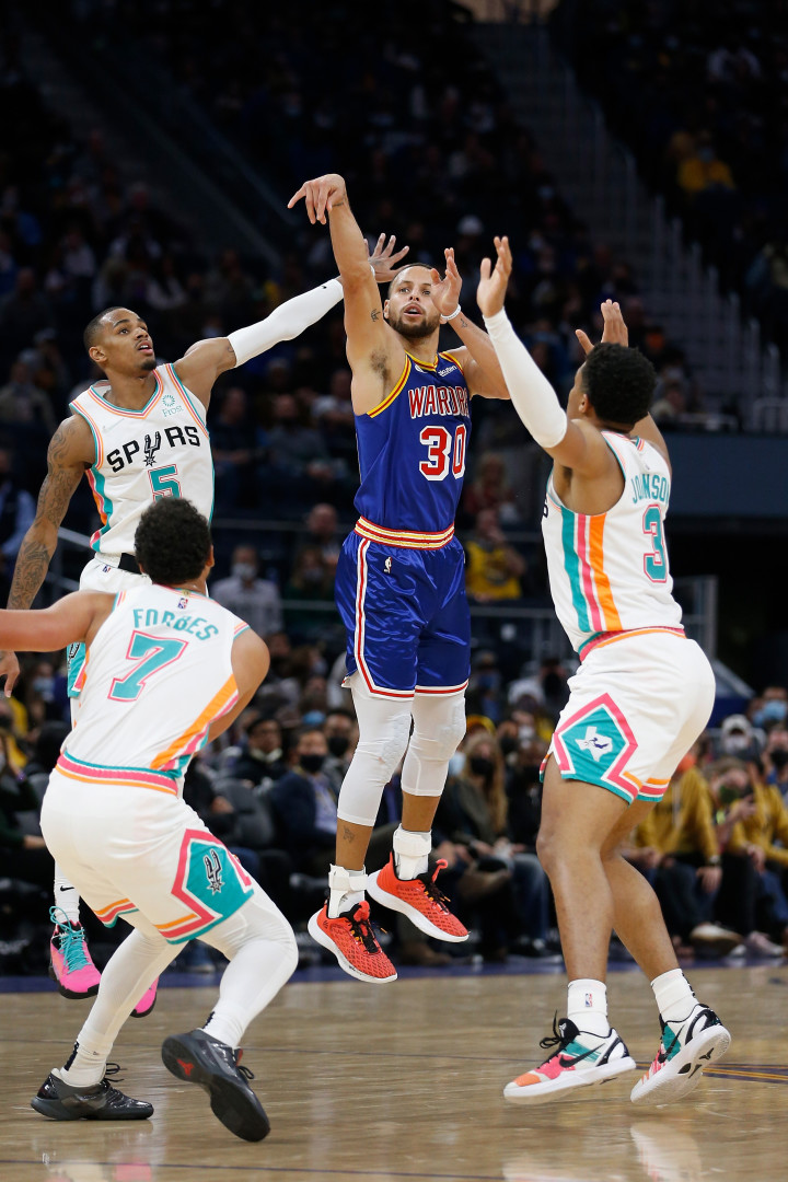 Stephen Curry mid air as he shoots for the hoop surrounded by three opposition players.