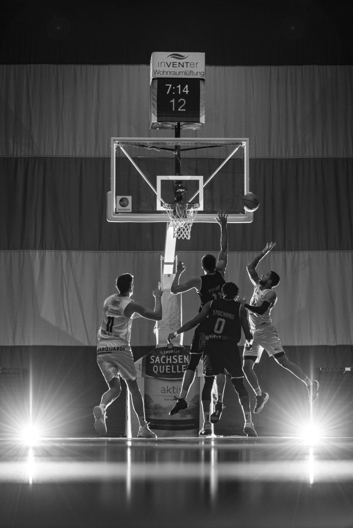 Black & White photograph of basketball players around a hoop as one opponent shoots his shot.