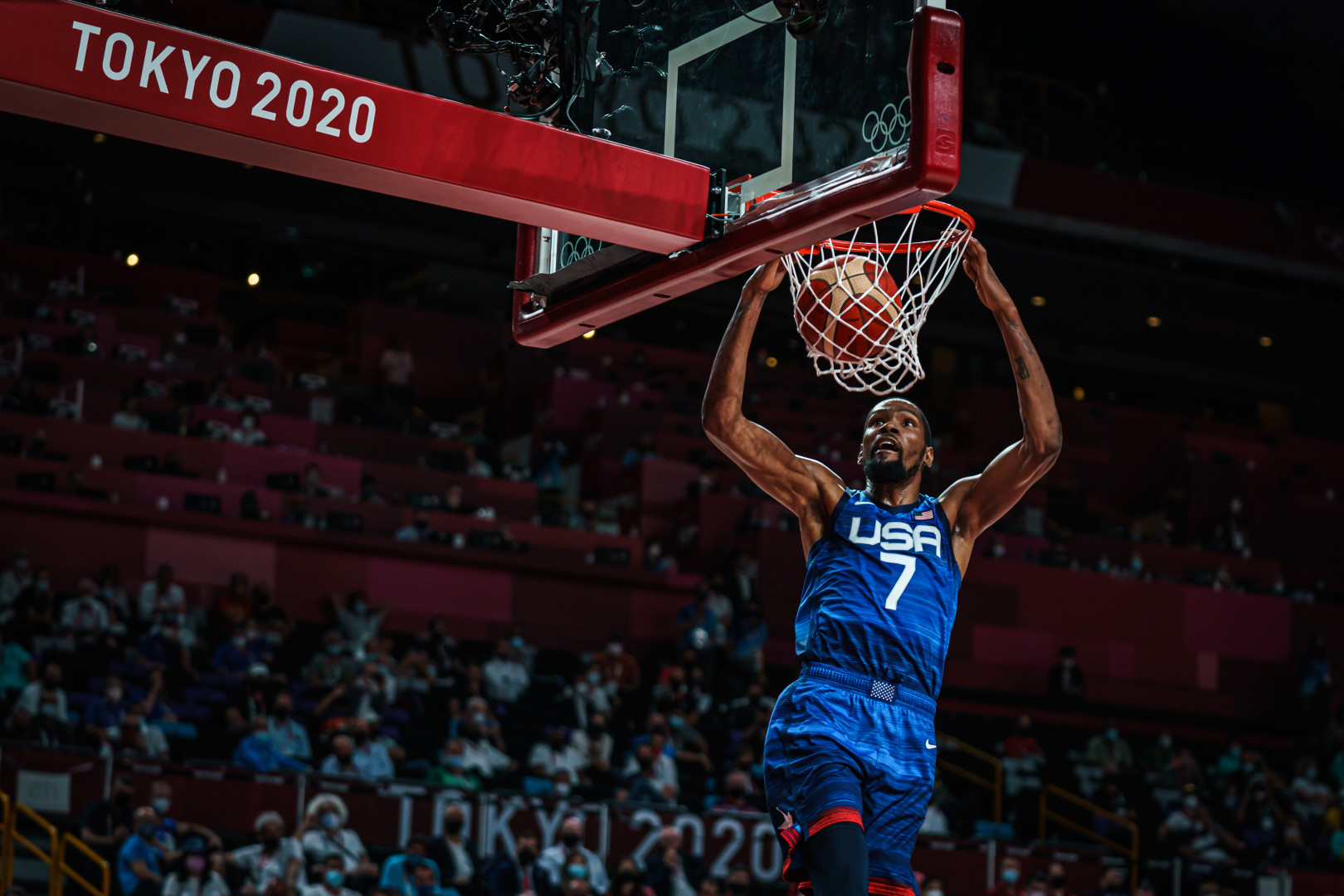 Number 7 for the USA basketball team holding onto the basketball hoop as he watches the ball go through the net.