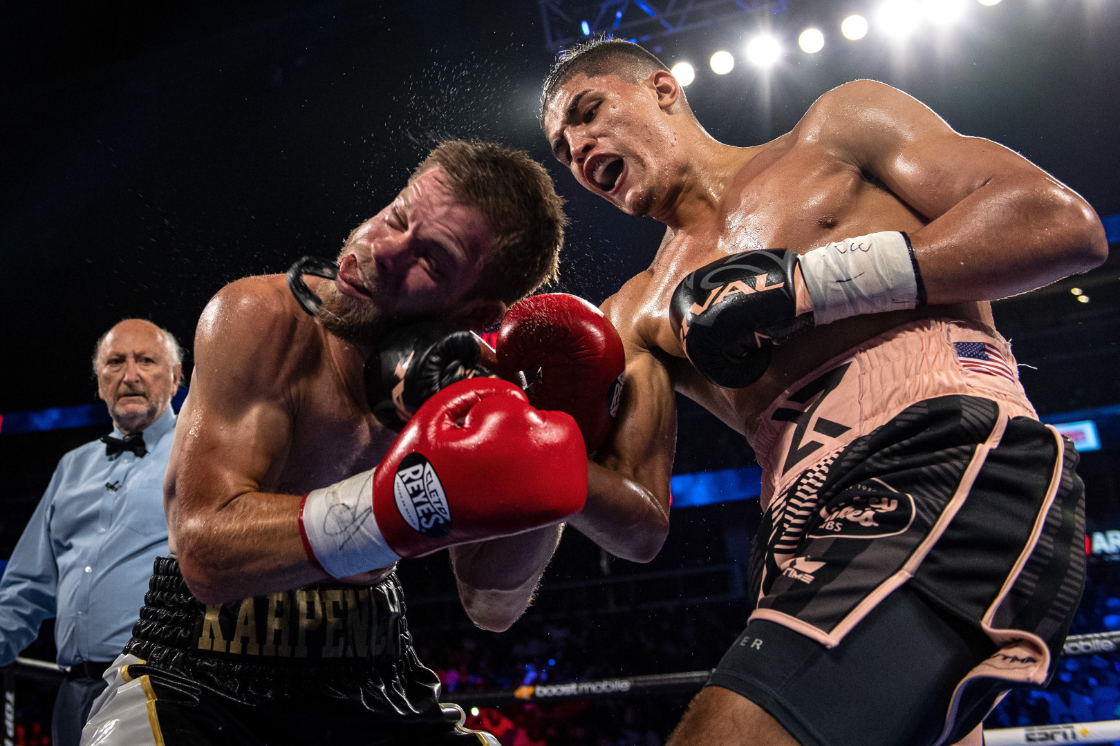 Boxer landing a hook to opposition boxer's face as referee watches on.