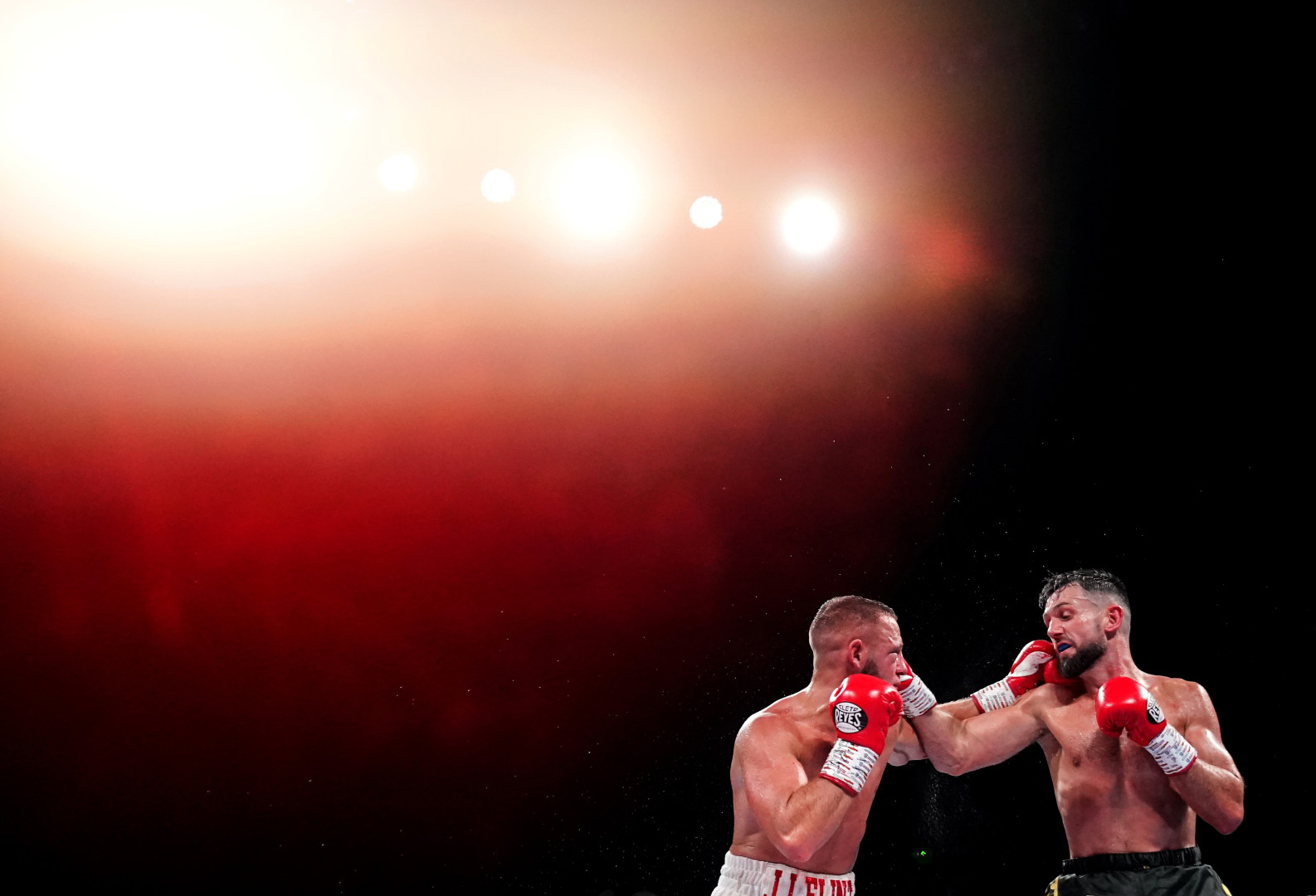 A haze of red light shining over two male boxers in the ring.